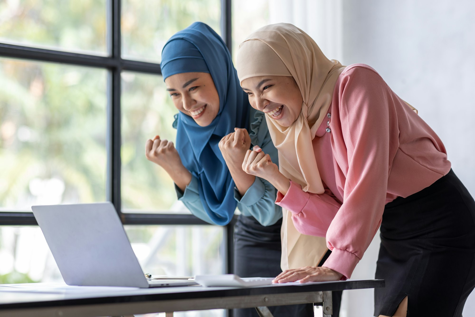 Young two beautiful smiling happy excited asian muslim women relaxing using laptop computer working